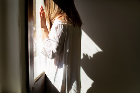 A woman standing up inside resting her hands on a window.
