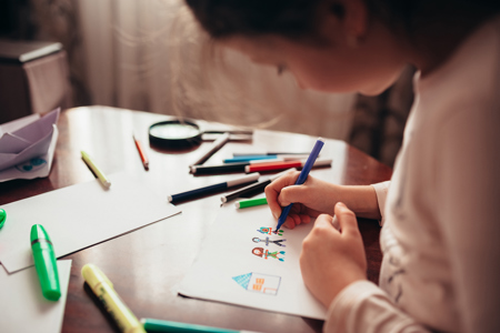 A child sitting at a table drawing on a piece of paper with a marker