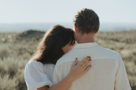 A couple wearing all white clothing embracing each other in a field of grass. 