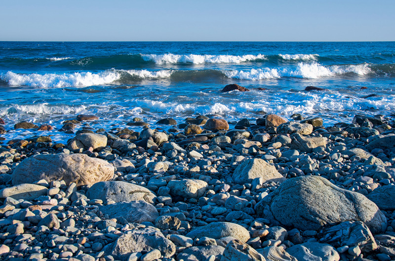 Waves crashing on a rocky beach under a clear blue sky