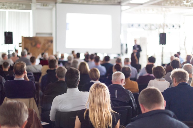 A large room full of people listening to someone talking. 