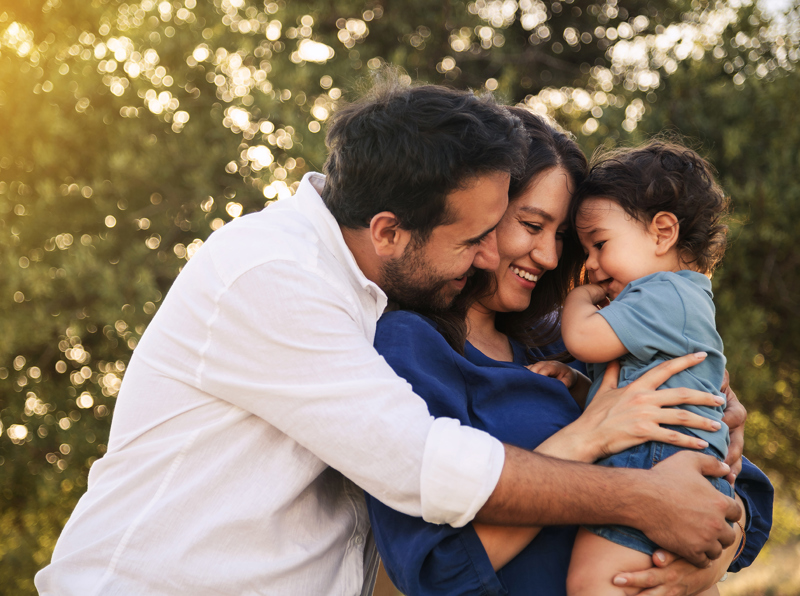 Happy parents embracing their toddler. They're outdoors and the light is golden