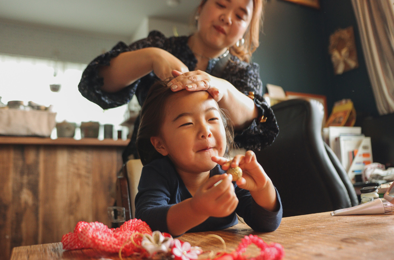 A mother brushing her daughter's hair while she sits at a table