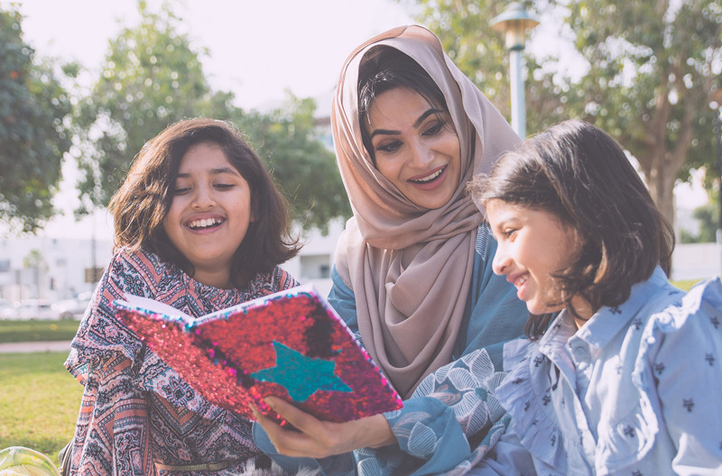 An Afghan mother and her two daughters reading a book in a park
