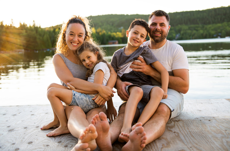 Two parents sitting with their children on a pier next to water. 