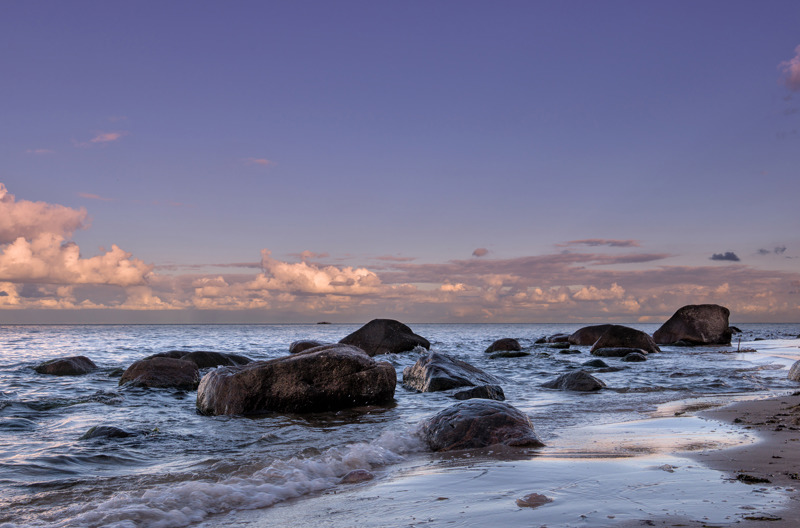Waves crashing on a rocky beach under a dusky purple and orange sky