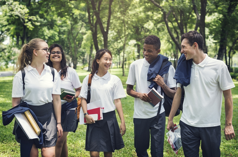 Five teenagers walking next to each other through a park